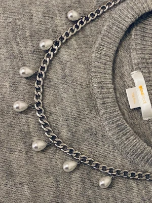 Kedjehalsband med droppformade pärlor - Snyggt halsband med en silverfärgad kedja och droppformade vita pärlor som hänger längs hela kedjan. Halsbandet har en modern och edgy känsla tack vare den grova länken och de coola pärldetaljerna. Perfekt för att lyfta vilken outfit som helst.