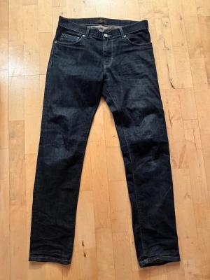 Mörkblå J Lindeberg jeans  - Snygga mörkblå jeans från J Lindeberg med klassisk femficksmodell och raka ben. Jeansen har en stilren look med kontrastsömmar och är tillverkade i kraftig denim. Perfekta för dig som gillar en enkel men trendig stil. Storlek 32/34