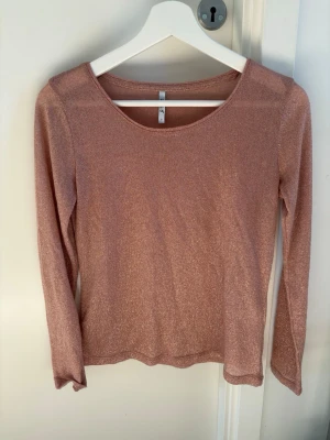 Glittrig rosa långärmad topp - Snygg rosa topp med glittrigt tyg och rund halsringning. Långärmad modell i stretchigt material som ger en bekväm passform. Perfekt för dig som vill sticka ut lite extra med en shimmer-effekt. Enkel och stilren design utan detaljer. Det finns dock ett väldigt litet streck på baksidan av tröjan men de syns knappt🩷
