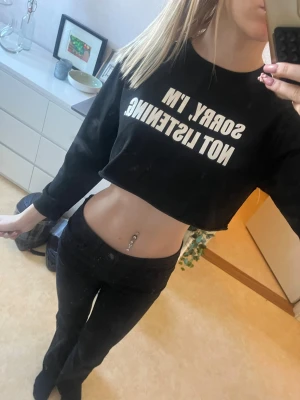Svart croppad topp med text - Svart croppad topp med vit text 'SORRY, I'M NOT LISTENING' på bröstet. Toppen har långa ärmar och en relaxed passform, perfekt för en chill och edgy stil. Materialet känns som bomull eller polyester.