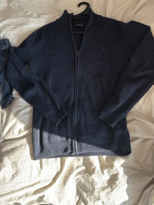 Mörkblå ziptröja  - Mörkblå ziptröja från med hög krage och hel dragkedja framtill. Tröjan är ribbstickad i bomullsmix och har långa ärmar samt ribbade muddar vid ärmslut och nederkant. Perfekt för lager på lager och enkel att matcha.