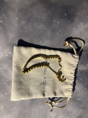 Guldigt pärlarmband Michael Kors - Snyggt armband från Michael Kors i guldfärgad metall med pärldetaljer och en elegant platta med logga. Justerbar kedja för perfekt passform. Kommer med original dustbag!