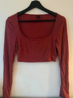 Rostbrun croppad topp  - Trendig croppad topp från SHEIN i en snygg rostbrun färg. Toppen har lång ärm, rundad djup urringning och är tillverkad i ett mjukt bomullsmaterial. Perfekt att styla med höga jeans eller kjol.