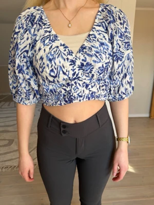 Blåvit croppad blus med puffärm - Säljer en croppad blus med blått och vitt mönster och puffiga korta ärmar. Toppen har v-ringning och resårdetalj i ryggens  nederkant. Perfekt för dig som vill ha en trendig och luftig topp till sommaren. Använd ett fåtal gånger. 