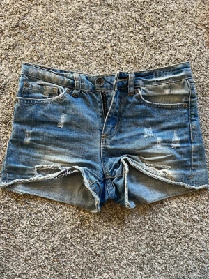 Blå slitna jeansshorts - Snygga vintage blå jeansshorts med slitna detaljer. Perfekta för i sommar.