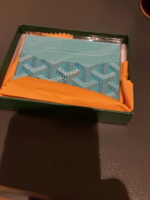 Turkos korthållare från Go4ard - Snygg turkos korthållare från Go4ard med deras ikoniska mönster och logga framtill. Tillverkad i läder med flera kortfack och stilren design. Perfekt för dig som vill ha något unikt och trendigt i fickan.