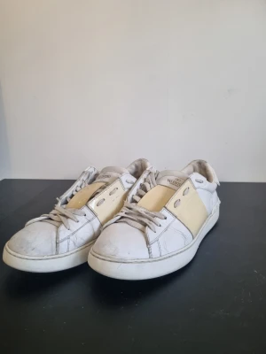 Valentino open - Snygga vita sneakers från Valentino Garavani med beige detalj på sidan. Klassisk låg modell med rund tå, vita skosnören och gummisula. Tillverkade i läder för en exklusiv känsla och stilren look.