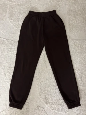 Bruna mjukisbyxor med resår - Bruna mjukisbyxor med resår i midjan och vid bensluten. Klassisk rak passform och sidofickor. Perfekta för en avslappnad stil. Materialet känns mjukt och bekvämt mot huden.