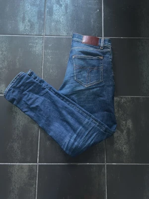 Mörkblå slim fit jeans - Snygga mörkblå slim fit jeans med klassisk femficksdesign och kontrastsömmar. Jeansen har en läderpatch bak i midjan och är tillverkade i denim med lätt stretch för extra komfort. Perfekta för en avslappnad och trendig look. 29/32 men kort i passformen så mer 30 i längd