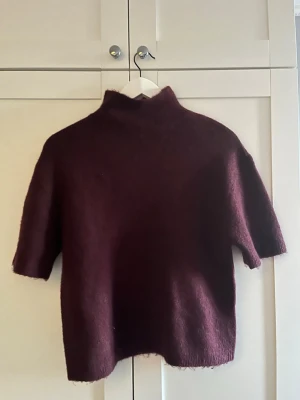 Vinröd stickad tröja  - Mysig vinröd stickad tröja från Gina Tricot i ullblandning. Tröjan har halvpolo och korta ärmar, perfekt för lager på lager. Enkel och stilren design som passar till många olika looks. Har bara används fåtal gånger