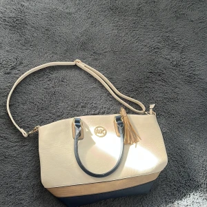 Beige och marinblå Michael Kors väska - Snygg handväska från Michael Kors i beige men dragkedjan har gått sönder så den har ingen drag grej i den.