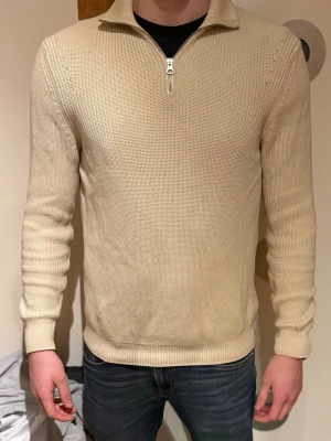 Beige Halfzip från Zara - Snygg beige stickad tröja med halfzip och ståkrage. Tröjan har lång ärm och ribbade muddar vid ärmslut och nederkant. Perfekt för lager-på-lager och enkel att matcha med jeans eller chinos. (Modellen är 190cm, 88 kg)