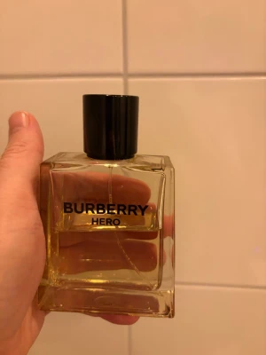 Burberry Hero parfym - Burberry Hero parfym i en stilren, fyrkantig glasflaska med svart lock. Flaskan är transparent med guldfärgad vätska och tydlig Burberry-logga på framsidan. Perfekt för dig som gillar klassiska och eleganta dofter. Ca 50% kvar