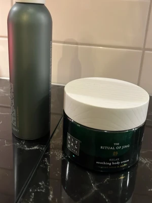Rituals body cream & duschskum - Säljer ett set från Rituals med en grön burk The Ritual of Jing Relax soothing body cream (vit lock) och en grå flaska The Ritual of Chadō duschskum. Lyxiga produkter med fräscha dofter och snygg design, perfekta för dig som vill unna dig lite extra self-care.