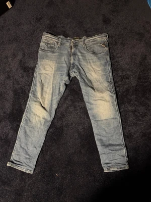 Ljusblå slim fit jeans från Replay - Snygga ljusblå jeans från Replay med slim fit passform och klassisk femficksdesign. Jeansen har slitna detaljer och ljusa partier framtill och baktill för en trendig look. Perfekta för dig som gillar en avslappnad men stilren stil.