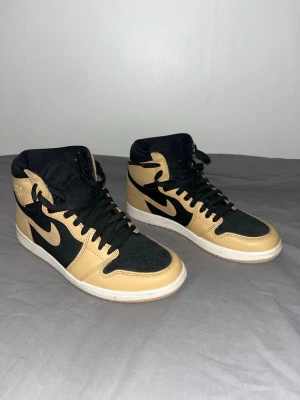 Jordan 1 Retro High OG svart/beige - Säljer ett par Jordan 1 Retro High OG i svart och beige, perfekt nu inför vår/sommaren. Skorna är ej creasade och har ej några synliga defekter förutom smuts som nu är borttaget! Skorna skickas i orginallådan. (Medföljer ett par röda snören) Skorna går också att hålla och sedan sälja vidare då dem nästan är helt nya. Skriv vid frågor osv!