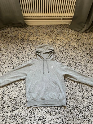  Nike S - Snygg grå hoodie från Nike med klassisk logga på bröstet. Hoodien har huva med dragsko och en stor magficka framtill. Perfekt för en avslappnad och sportig stil. Tillverkad i mjukt material för extra komfort.