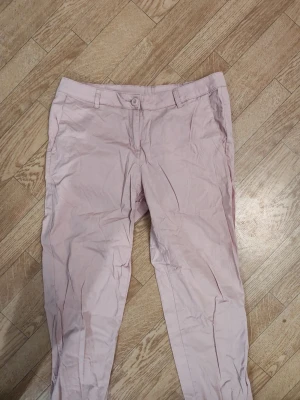 Gammelrosa chinos byxor dam stl 40 - Snygga gammelrosa chinos/byxor med klassisk passform och raka ben. Byxorna har hällor för bälte, knapp och dragkedja framtill samt sidfickor. Perfekta för en avslappnad men stilren look. Materialet känns lätt och bekvämt. Dam stl 40