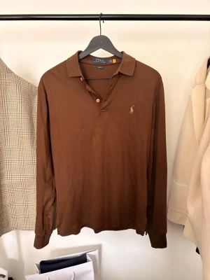 Brun långärmad polotopp från Polo Ralph Lauren - Snygg brun långärmad polotopp från Polo Ralph Lauren i slim fit-modell. Storlek M men passar mer S.