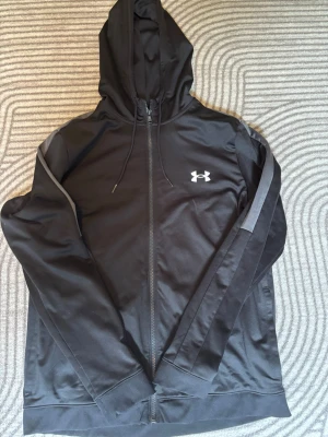 Svart hoodie från Under Armour - Svart hoodie från Under Armour med dragkedja och huva i Storlek L pris går att diskutera 