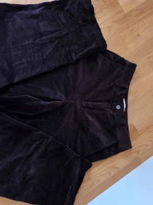 Bruna manchesterbyxor Comptoir des Cotonniers - Mörkbruna manchesterbyxor från uniqlo med barrel leg passform och normal midja. Byxorna har tydlig manchesterstruktur och stängs med knapp och dragkedja. Perfekta för dig som gillar en tidlös och avslappnad stil.