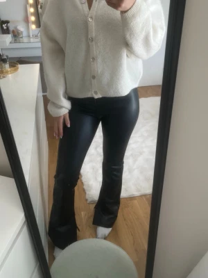 Svarta utsvängda byxor i skinnimitation - Snygga svarta byxor i skinnimitation med utsvängda ben och slits från Bershka.. Endast använda en gång så i nyskick
