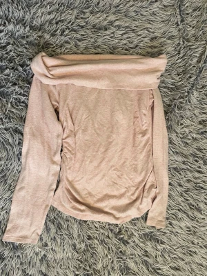 Ljusrosa offshoulder topp - Trendig ljusrosa offshoulder topp med lång ärm och bred krage som kan vikas ner över axlarna. Tillverkad i mjukt material med en slim passform som sitter snyggt på kroppen. Perfekt för dig som vill ha en stilren och feminin look.