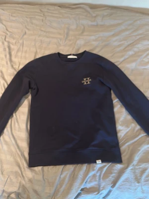 Mörkblå sweatshirt från Les Deux - Mörkblå sweatshirt från Les Deux med rund halsringning och diskret broderad logga på bröstet. Tröjan har långa ärmar och ribbade muddar vid hals, ärmslut och nederkant. Perfekt för en avslappnad och stilren look. Skriv vid frågor:)