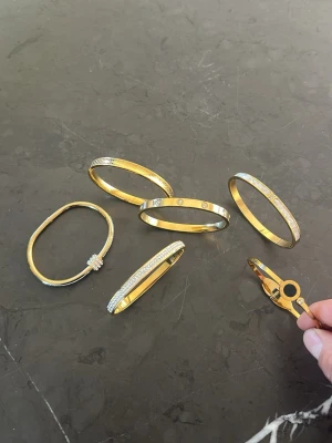  6st 18K Guld i pläterad armband med stenar - Säljer flera snygga armband i guldfärgad metall, vissa med gnistrande stenar och detaljer. Några har klassisk oval form och andra är runda, med inslag av pärlor och dekorativa mönster. Perfekta för att lyfta din stil med en lyxig touch. 
