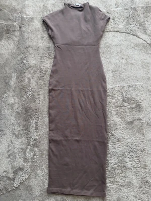 Brun midiklänning från Zara - Säljer en stilren brun midiklänning från Zara med korta ärmar och hög hals. Klänningen har en figurnära passform och är tillverkad i mjuk bomull, perfekt för en enkel och trendig look.