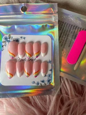 Press-on naglar med regnbågsfrench - Snygga press-on naglar i mandelform med ljusrosa bas och färgglad regnbågsfrench i vitt, orange, gult, grönt och rosa. Kommer i förpackning med tillbehör som fil och träpinne. Perfekt för dig som vill ha trendiga och färgstarka naglar snabbt.