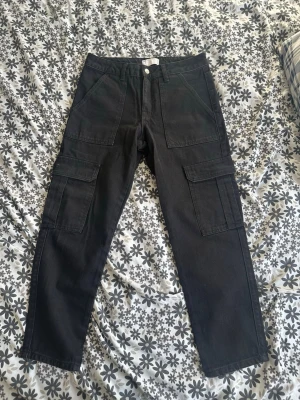 Svarta cargobyxor från ASOS DESIGN - Snygga svarta cargobyxor från ASOS DESIGN med raka ben och flera stora fickor på sidorna. Tillverkade i bomullstyg och perfekta för en avslappnad streetstil. Klassisk cargomodell med knapp och dragkedja framtill.