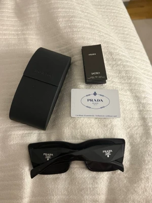 Svarta solglasögon från Prada - Snygga svarta solglasögon från Prada med rektangulära bågar och mörka glas. Kommer med fodral. (aa)
