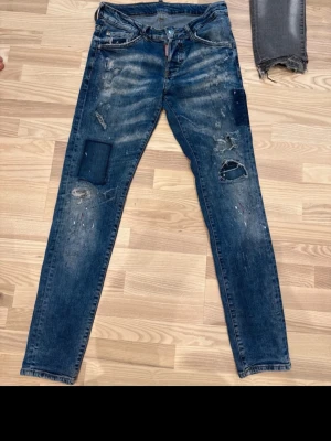 Dsquared2 jeans  - Säljer ett par blå jeans med skinny fit och coola slitningar samt patchdetaljer på benen. Jeansen har en klassisk femficksmodell och dragkedjegylf. Perfekta för dig som gillar en trendig och avslappnad streetstil.