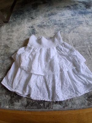 Vit volangkjol från Zara - Supersöt vit kjol från Zara med volanger och broderade hål. Kjolen har smock i midjan och är perfekt för varma dagar. Lätt och luftig med fina detaljer som ger en romantisk känsla.