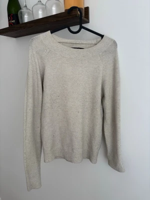 Beige stickad tröja från Vero Moda - Mysig beige stickad tröja från Vero Moda med rund halsringning och långa ärmar. Tröjan har ribbstickade muddar vid ärmslut och nederkant, perfekt för lager-på-lager. Enkel och stilren design som passar till det mesta.