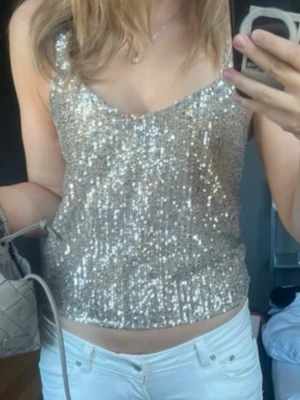 Glittrig guldig paljettopp - Snygg glittrig topp i guld med paljetter över hela. Linnemodell med smala axelband och lätt v-ringad halsringning. Perfekt för dig som vill sticka ut och glänsa lite extra. Passar till både jeans och kjol.