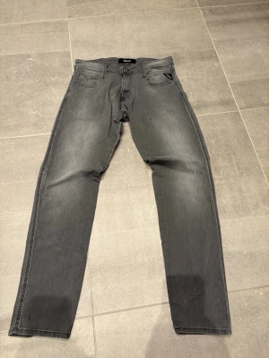 Gråa jeans från Replay - Snygga gråa jeans från Replay med klassisk femficksdesign och raka ben. Jeansen har en diskret tvättad look och svarta detaljer vid fickorna. Använda ungefär 5 gånger.