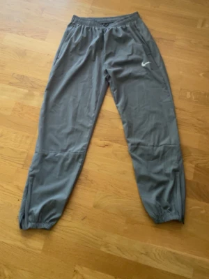 Grå mjukisbyxor från Nike - Säljer ett par grå mjukisbyxor från Nike med resår i midjan och vid bensluten. Byxorna har en avslappnad passform och sidofickor. Perfekta för chill dagar eller träning. Nike-logga broderad på vänster ben.