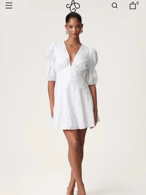 ADOORE klänning - Sicily dress  - Supersöt vit kort klänning med puffärmar och v-ringning. Klänningen har knappar framtill, markerad midja och lätt utställd kjol. Använd 2 gånger och är perfekt för sommarens alla tillfällen! 