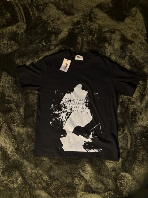 Maison Margiela t-shirt - Cool svart t-shirt från Maison Margiela med vit grafisk print och logga framtill. Klassisk passform med korta ärmar och rund halsringning. Tillverkad i mjuk bomull som känns skön mot huden. Perfekt för dig som gillar streetstyle och designerplagg. Kom privat om du har frågor!