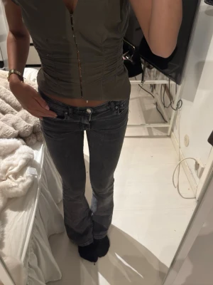 Grå bootcut jeans med låg midja - Snygga grå bootcut jeans med låg midja och klassisk femficksdesign. Jeansen har en lätt tvättad look och sitter tajt över låren för att sedan släppa ut vid bensluten. Perfekta för en trendig och avslappnad stil.