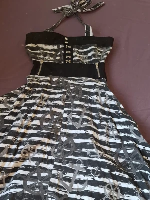 Klänning Vixxsin - Svartvit klänning från Vixxsin med randigt mönster och stora ankare över hela tyget. Halterneck. Perfekt för dig som gillar alternativ stil och unika detaljer. 