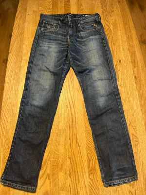 Mörkblå raka jeans från Replay  - Snygga mörkblå jeans från Replay med raka ben och klassisk femficksdesign. Jeansen har slitningar och ljusare partier framtill för en cool, använd look. Tillverkade i denim med detaljerade sömmar och logotyp på bakfickan.