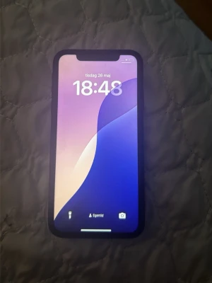 Svart iPhone XR med glasbaksida - Säljer en svart iPhone XR från Apple med stilren design och rundade kanter. Telefonen har en stor skärm med tunn ram och baksida i glas med Apple-loggan. Perfekt för dig som vill ha en snygg och modern mobil.