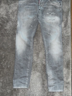 Ljusgråa jeans från DSQ2 - Snygga ljusgrå jeans från DSQ2 med slitna detaljer och diskreta revor framtill. Jeansen har en klassisk femficksmodell och en röd DSQ2-lapp bak i midjan. Perfekta för en trendig och avslappnad stil.
