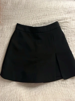 Svart kostymkjol - Stilrena svarta kostym kjol med en snygg slits framtill och shorts på insidan. Dragkedja på sidan. 