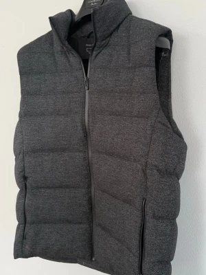Mörkgrå dunväst med dragkedja - Snygg mörkgrå dunväst med hög krage och hel dragkedja framtill. Exklusiv Porsche design, använd noll gånger då den är för stor. Utmärkt skick och stilren! 🙌✌️