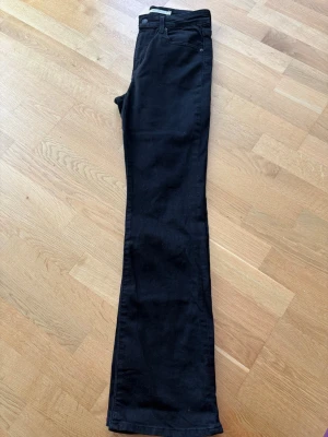 Svarta bootcut jeans Levi’s 725  - Snygga svarta bootcut jeans från Levis modell 725 med klassisk femficksdesign och hög midja. Jeansen har en smal passform upptill och utsvängda ben. Perfekta för dig som gillar en trendig och stilren look. Storlek 28x32!!