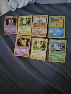 Samling Pokémonkort vintage 1990 talet - Säljer en samling med sju klassiska Pokémonkort, bland annat Pikachu, Kadabra, Dugtrio och Nidorina. Korten är i färgerna gul, lila, blå och grön med ikoniska illustrationer och originaldesign. Perfekt för dig som gillar samlarkort och nostalgi från Pokémon. 1990 talet 